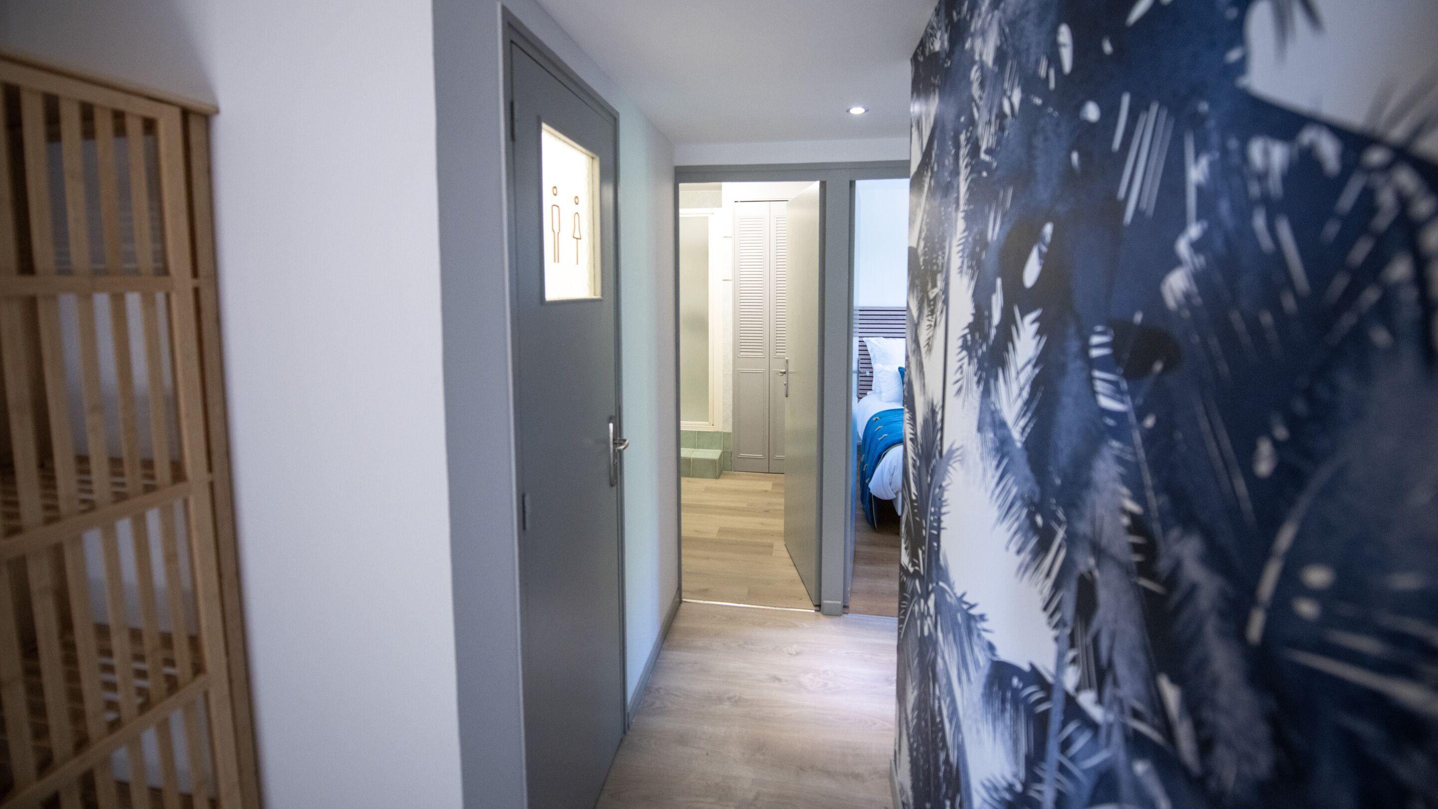 Un pasillo con puerta de madera, una cama azul y un papel tapiz estampado.