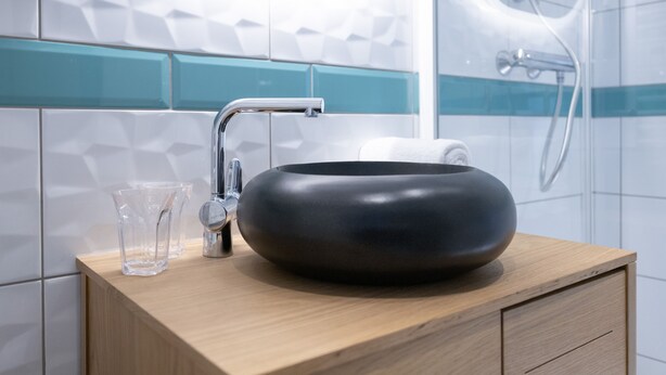 Un baño moderno con un lavabo tipo cuenco negro, un grifo y un vaso sobre el mostrador.