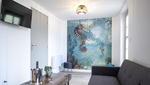 Een moderne woonkamer met een grote muurschildering van een zeepaard, een wandgemonteerde flatscreen televisie, een houten salontafel en een grijze bank.