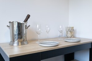 Un comptoir de cuisine sur lequel se trouve un récipient en acier inoxydable contenant une bouteille, quatre verres à vin et deux assiettes.