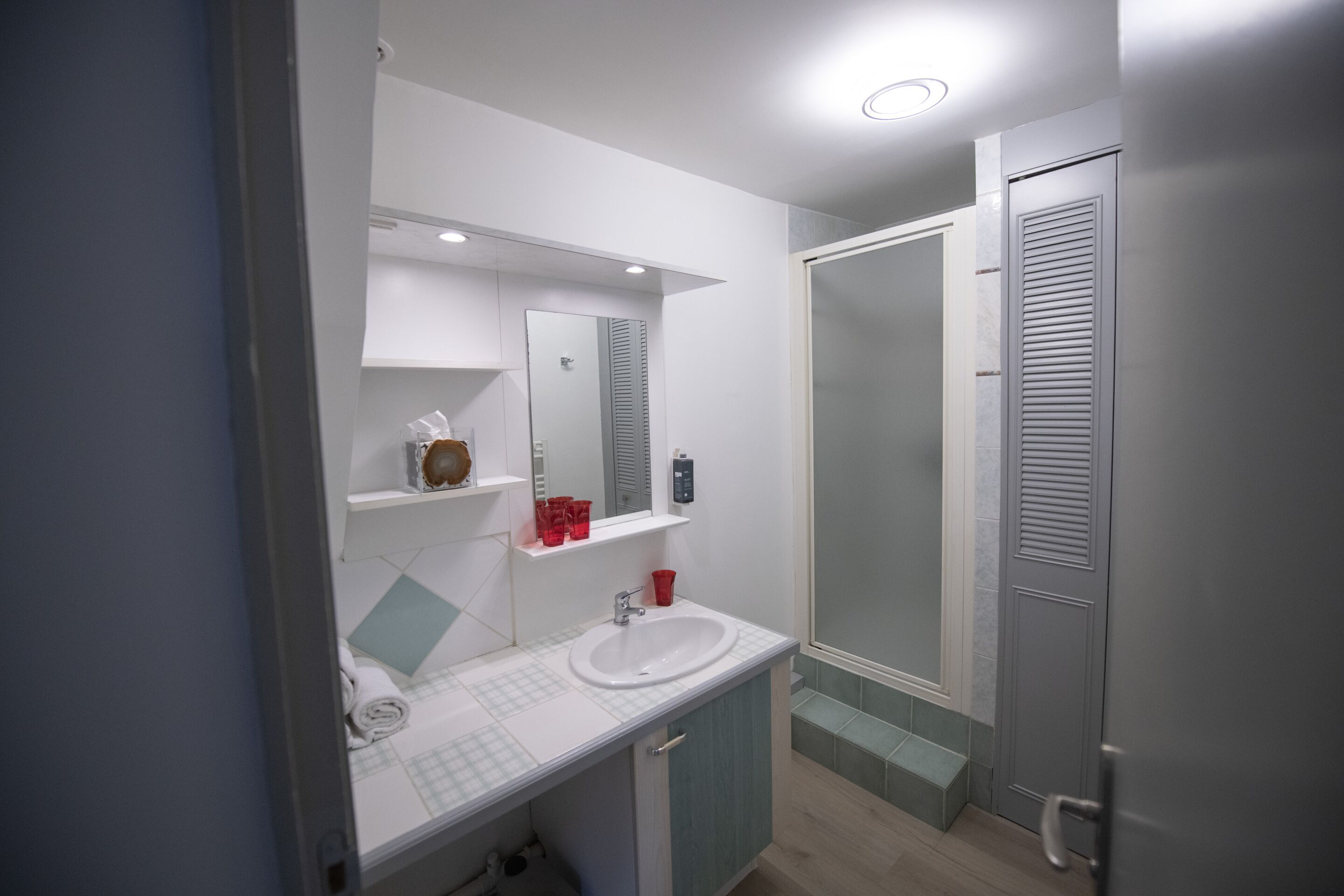 A modern bathroom with a white sink, mirror, and shelves.