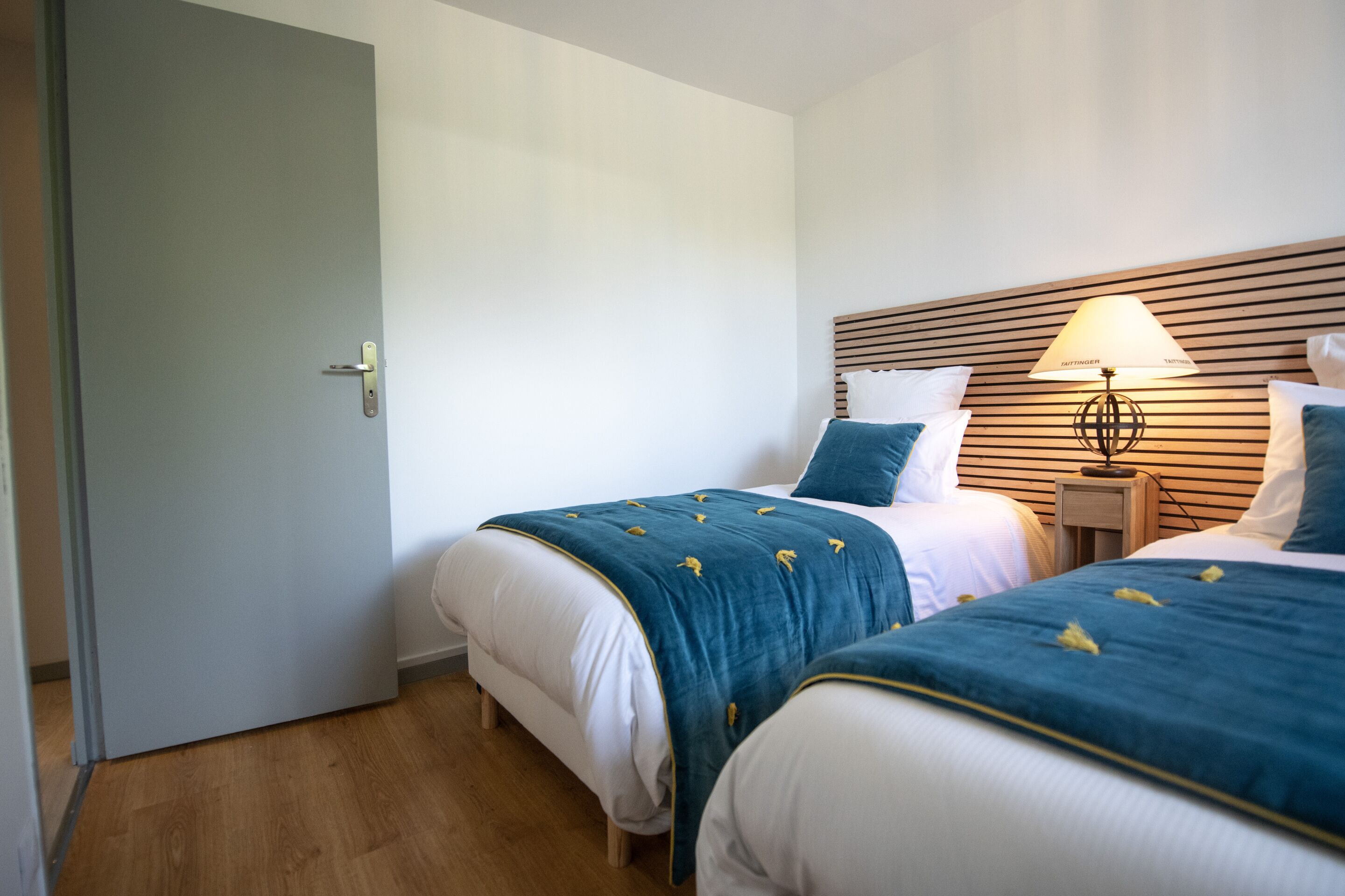 Ein Hotelzimmer mit zwei Betten, einem hölzernen Kopfstück, einem Nachttisch mit Lampe und einer Tür.
