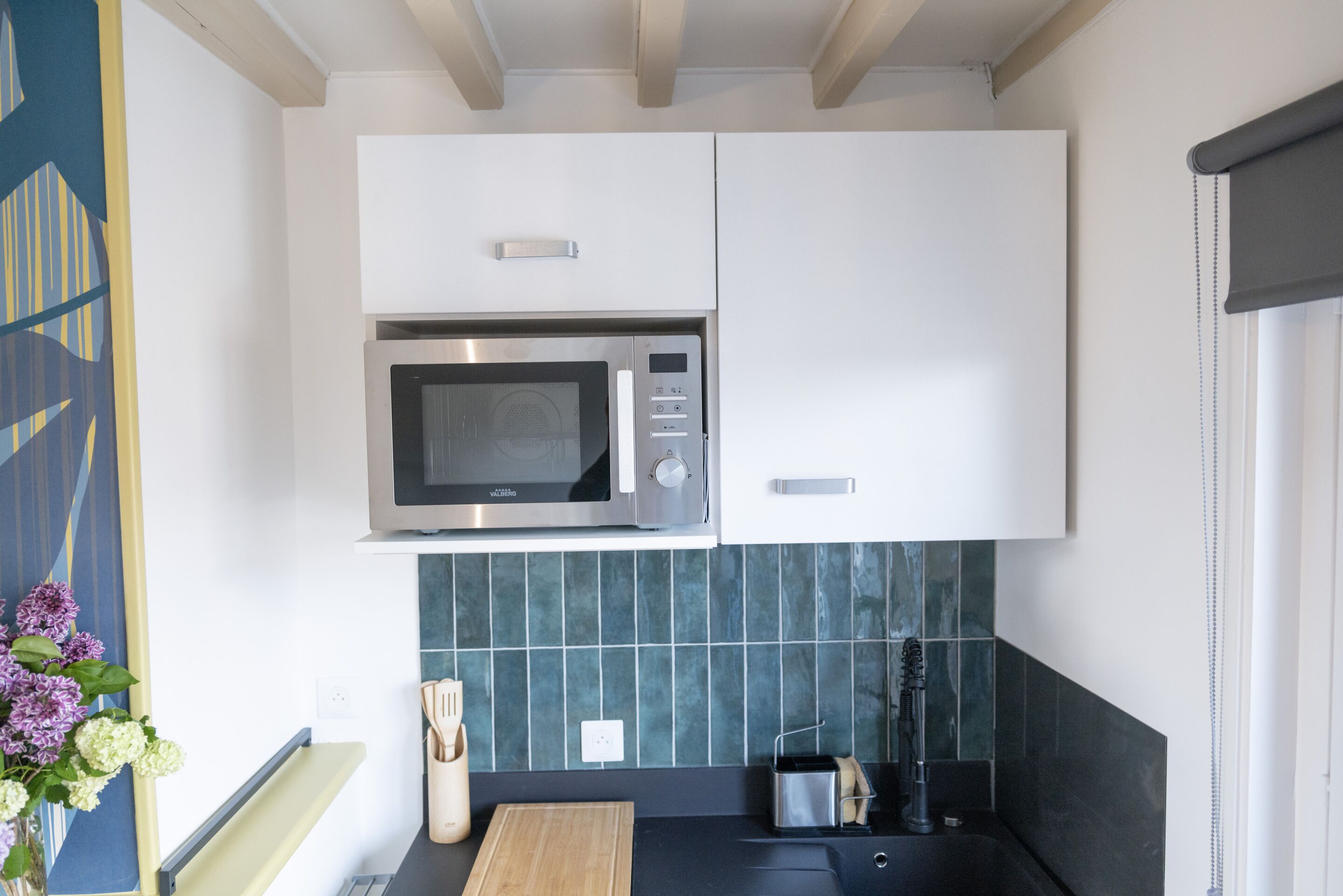 Et moderne køkken med hvide skabe, en stålfarvet mikroovn og en backsplash med grønne fliser.