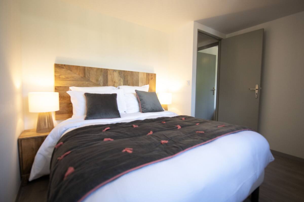 Un lit bien fait, recouvert d’une couvre-lit à motifs sombres, avec deux lampes de chevet et une tête de lit en bois.