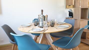 A round dining table with four blue chairs, a silver pitcher, and several wine glasses.