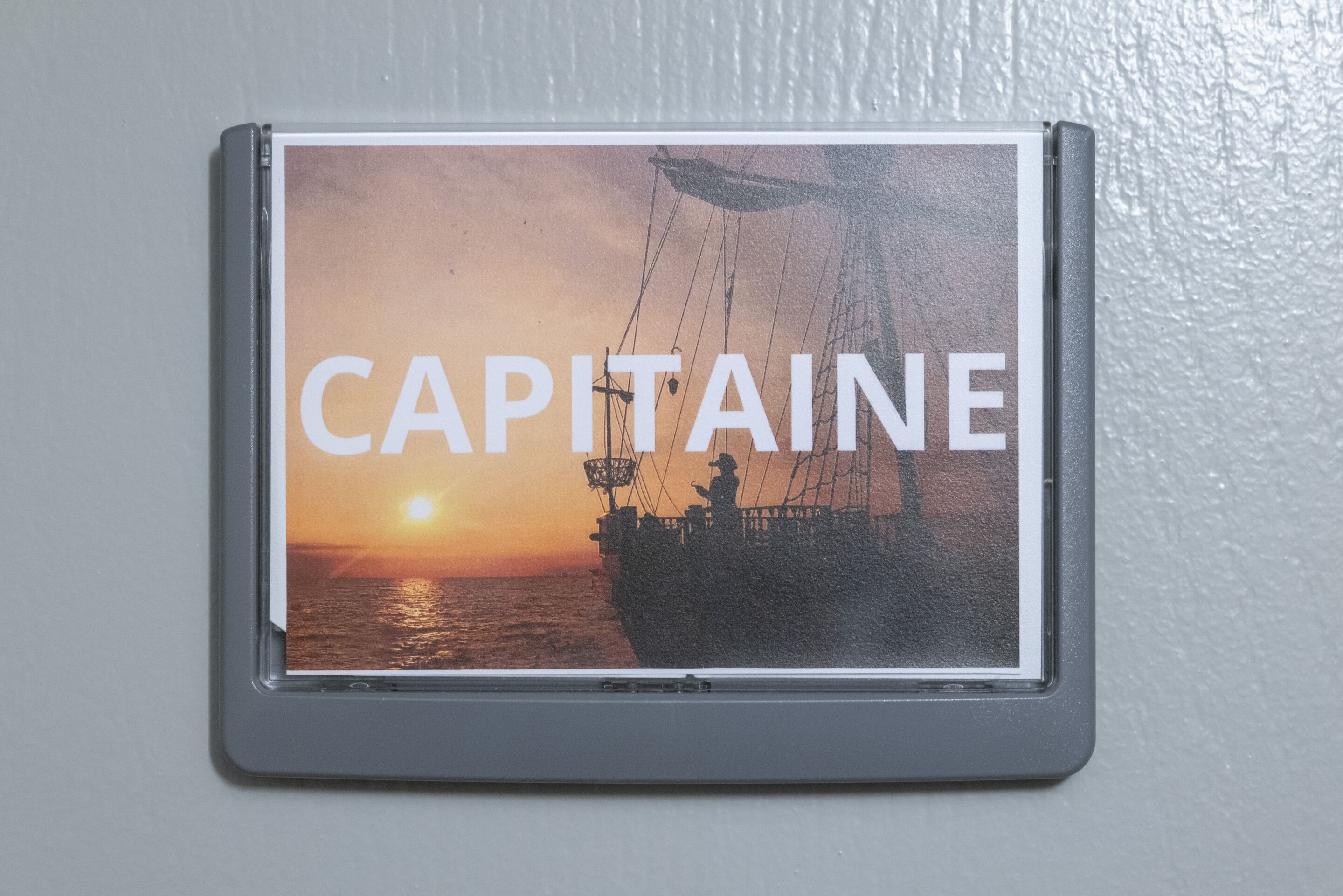 Een lijst met een foto van een schip bij zonsondergang, met daarop de tekst 'CAPITAINE'.
