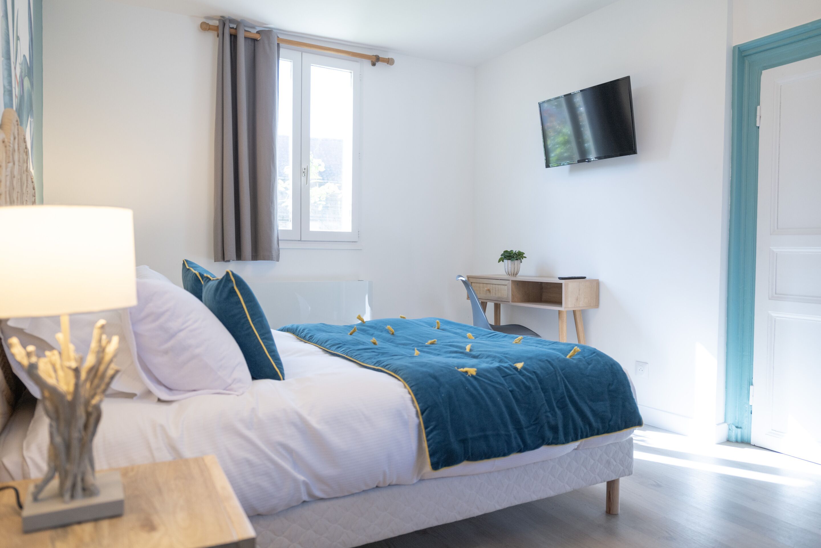 Une chambre à coucher avec un lit, une table de chevet, une lampe, une télévision et un bureau agrémenté d’une plante.