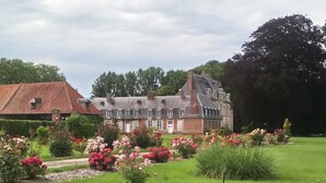 Een groot, historisch gebouw met een symmetrische gevel, omgeven door een verzorgde tuin met diverse bloeiende planten.