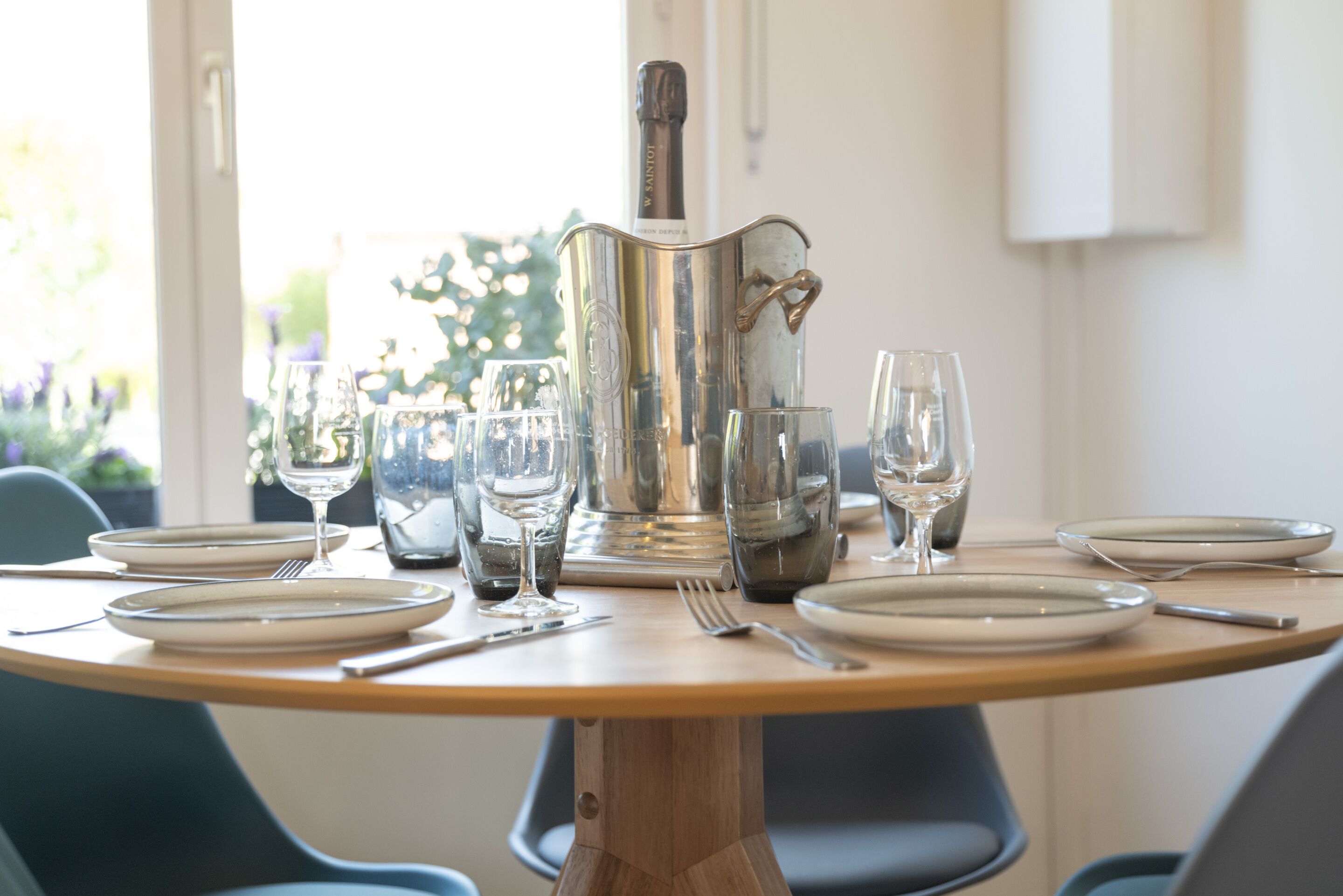 Une table à manger dressée avec des assiettes, des couverts et des verres à vin, et une bouteille de champagne placée au centre.