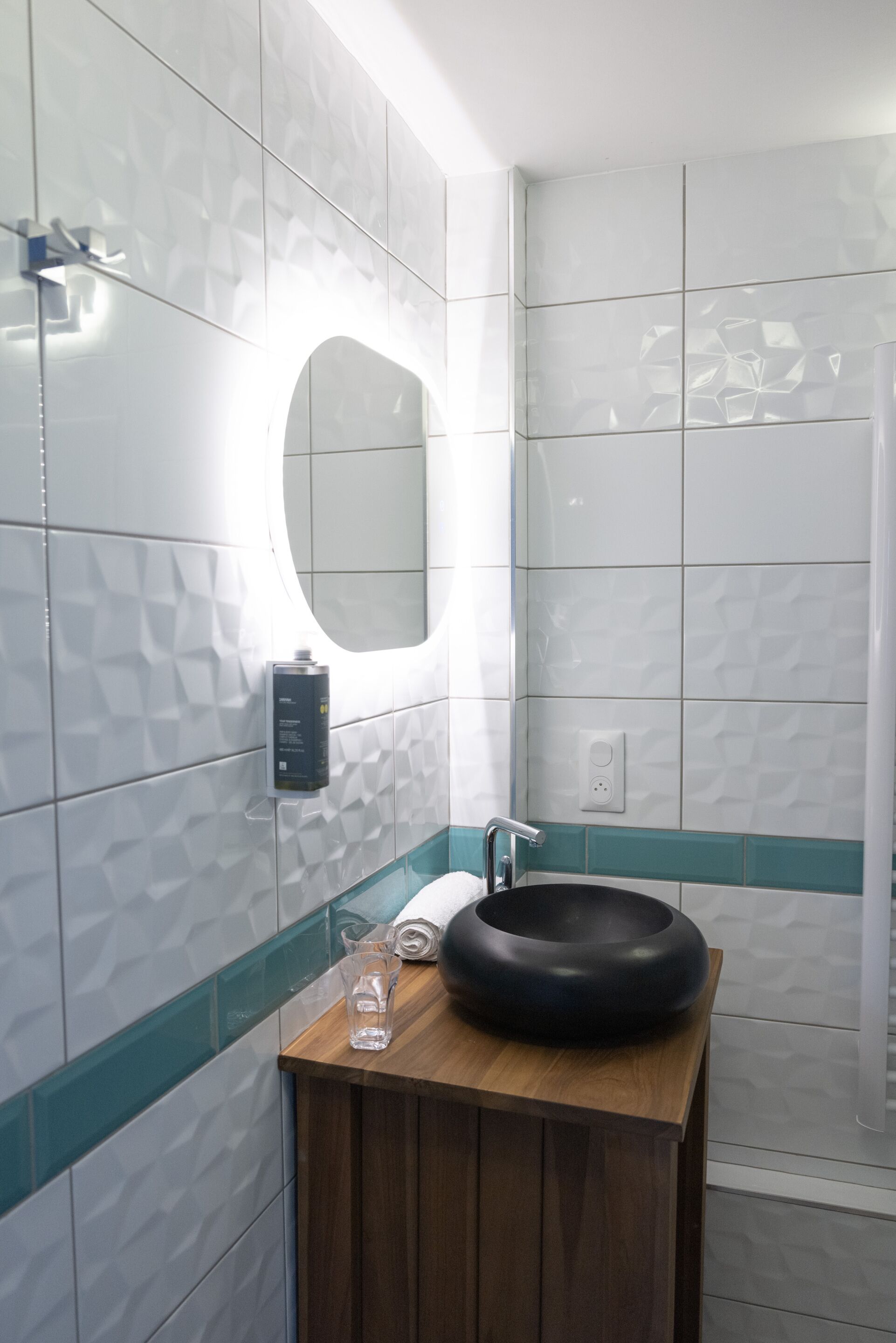 Un baño con tocador de madera, lavamanos negro, espejo y cabina de ducha con mampara de vidrio.