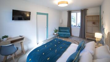 Un dormitorio con cama, escritorio, silla, televisor, ventana con cortinas y lámpara de noche.