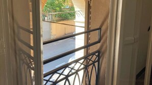 A view through a doorway with a metal railing, leading to an outdoor area with a paved surface and greenery.