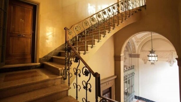 A grand staircase with ornate metal railings and a marble floor, leading to an upper level.