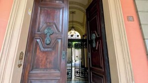 A wooden door with a brass handle and a decorative keyhole, leading to a gated entrance with a wrought iron gate.