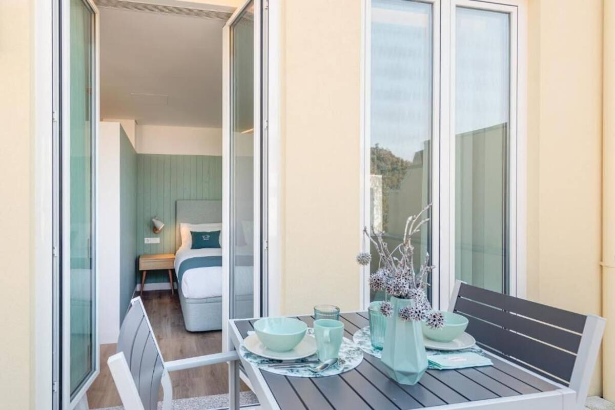 Ein Balkon mit Tisch für zwei Personen, ein Bett mit grünem Kopfteil und Blick auf die Landschaft.