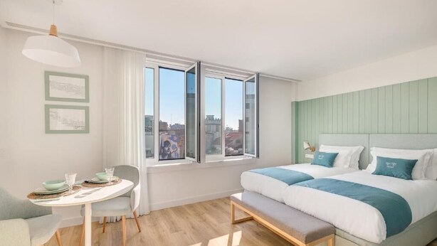 A modern bedroom with a large bed, a small table with chairs, and a bench. - 7 Bridges Estúdios (Porto)