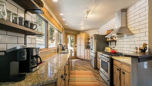 A modern kitchen with granite countertops, stainless steel appliances, wooden cabinets, and a large window providing natural light. - Elevated Home w/Hot Tub, Beautiful Views, Firepit, 3 King Bedrooms, Bunkroom (Angel Fire)