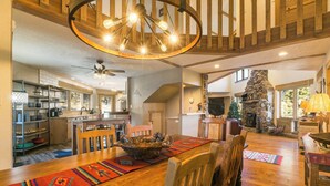 A spacious living area with a wooden dining table, chairs, and a stone fireplace. - Elevated Home w/Hot Tub, Beautiful Views, Firepit, 3 King Bedrooms, Bunkroom (Angel Fire)