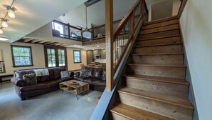 A spacious living area with a wooden staircase, leather sofas, and a high ceiling with exposed beams. - ⭐️Rustic Hill Country Barn retreat on acreage⭐️ (San Marcos)