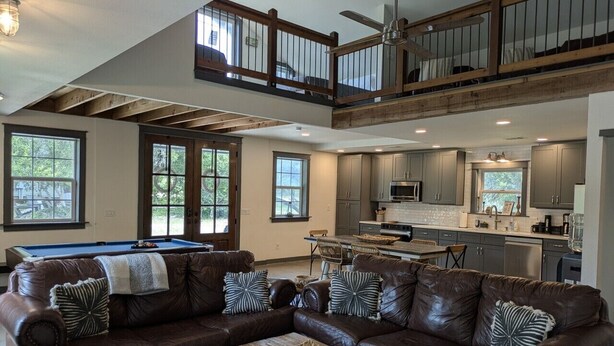 A spacious living area with a brown leather sectional sofa, a pool table, and a kitchen in the background. - ⭐️Rustic Hill Country Barn retreat on acreage⭐️ (San Marcos)