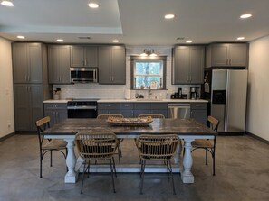 A modern kitchen with grey cabinets, a central island with chairs, and built-in appliances.
