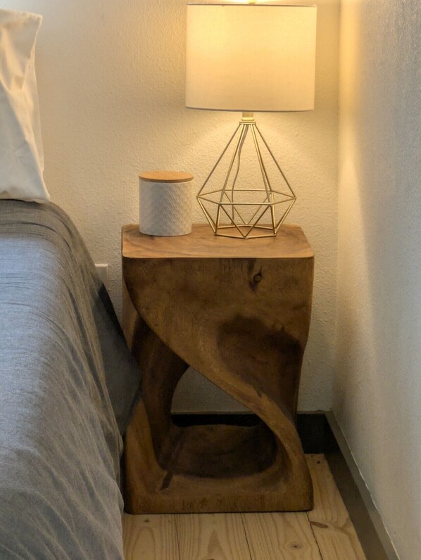 A bedside table with a lamp, a cylindrical container, and a geometric metal sculpture.