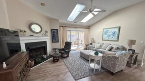 A living room with a fireplace, a ceiling fan, a sofa, a coffee table, and a view through a glass door. - Tranquility awaits, close to Wrightsville beach & downtown Riverwalk! (Wilmington)