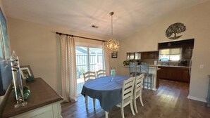 A dining area with a table and chairs, a kitchen in the background, and a ceiling light fixture. - Tranquility awaits, close to Wrightsville beach & downtown Riverwalk! (Wilmington)