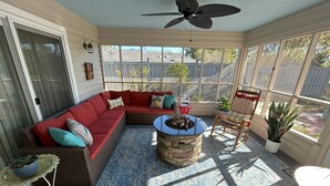 A sunroom with a red sectional sofa, a round table with a fire pit, and a ceiling fan. - Tranquility awaits, close to Wrightsville beach & downtown Riverwalk! (Wilmington)