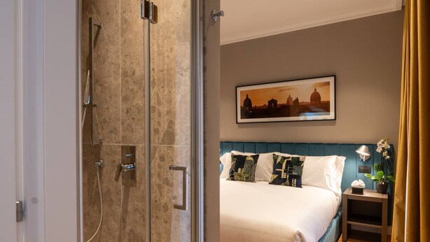 A hotel room with a bed, a nightstand, a lamp, and a framed picture on the wall. - Your room like in a 4-star Hotel (Roma)
