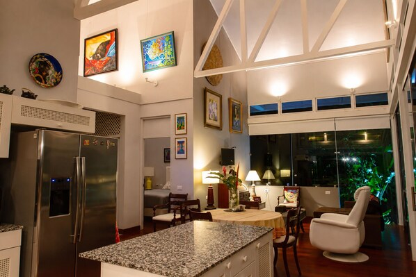 Una cocina moderna con refrigerador, encimera de granito, comedor con sillas y obras de arte en las paredes.