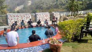 A group of people sitting around a pool with stone walls and a tiled floor. - Camp Aquaforest  (Rishikesh)