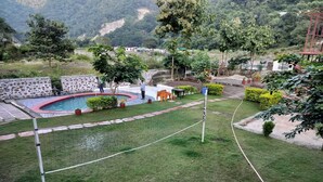 A well-maintained outdoor area with a swimming pool, stone walls, and various plants. - Camp Aquaforest  (Rishikesh)