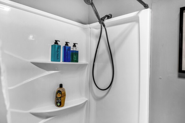 A shower area with a white bathtub, a handheld showerhead, and three shelves holding body wash bottles. - Modern 4-bedroom house near Lake Decatur (Decatur)