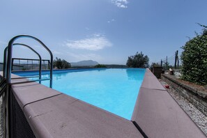 A swimming pool with a metal ladder, surrounded by a low stone wall and greenery.