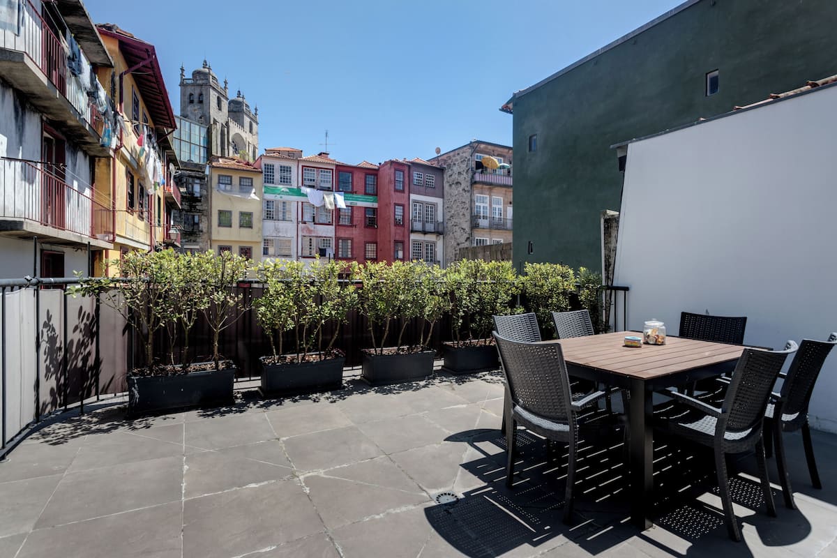 A patio with a table and chairs, surrounded by potted plants and a view of colorful buildings.