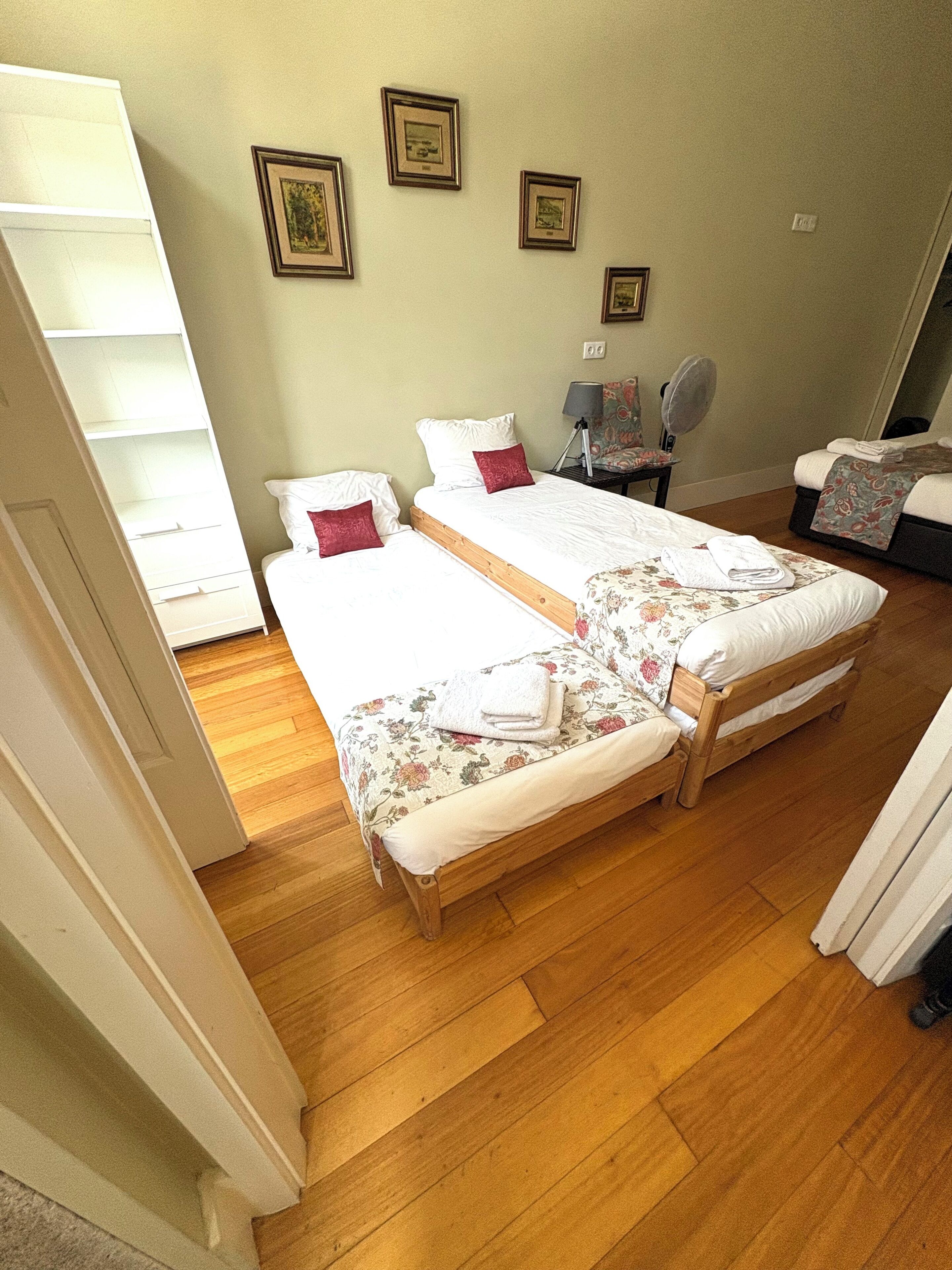 A bedroom with two single beds, a wooden floor, and a small table with a lamp.