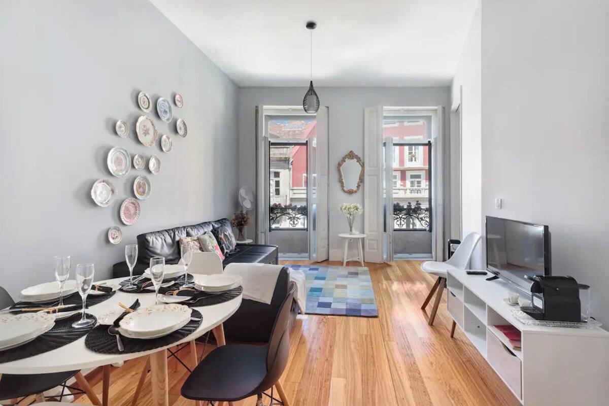 A modern living room with a dining area, a sofa, a TV, and a balcony with a view.