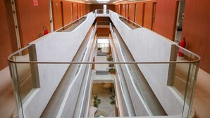 A modern hotel corridor with glass railings, a central staircase, and orange textured walls.
