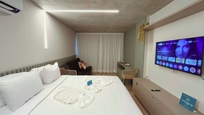 Een hotelkamer met een bed, bureau, stoel, televisie en een wandairconditioner.