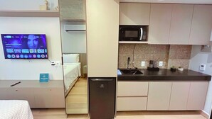 Una habitación de hotel compacta con kitchenette, una cama, un televisor y un refrigerador pequeño.