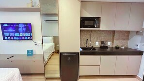 Une chambre d’hôtel compacte comprenant un coin cuisine, un lit, une télévision et un petit réfrigérateur.