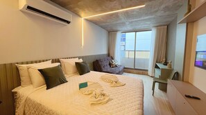 Hotellihuone, jossa on suuri sänky, työpöytä ja tuoli. Huoneessa on ikkuna, jossa on verhot, ja ikkunasta on näkymä ulos.