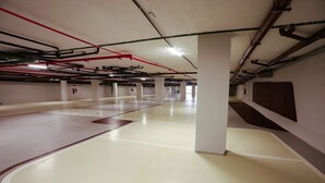 Un estacionamiento vacío con pisos blancos, tuberías rojas y negras en el techo y pilares blancos.