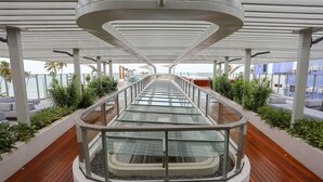 A modern outdoor corridor with glass railings, wooden flooring, and potted plants.