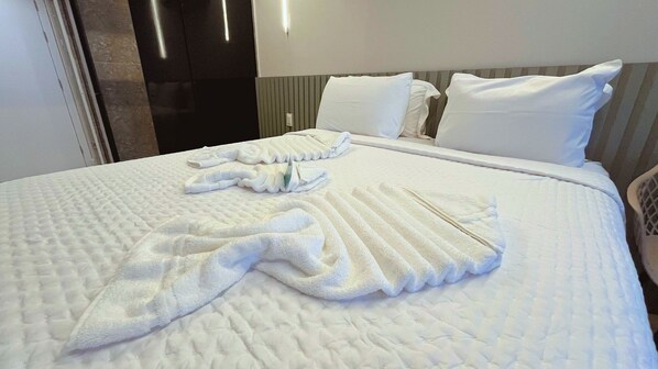 Een net opgemaakt bed met een witte quilt en handdoeken.