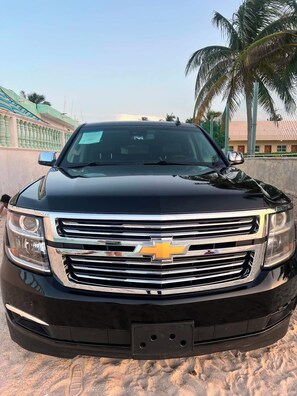 Ein schwarzes Chevrolet Fahrzeug parkt auf sandigem Untergrund, im Hintergrund Palmen und ein Gebäude.