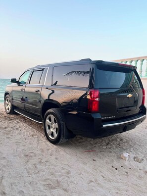 Ein schwarzer SUV parkt auf einem sandigen Strand, im Hintergrund ist ein klarer Himmel zu sehen.