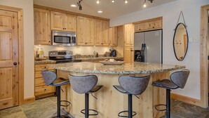 A kitchen with wooden cabinets, a granite countertop, a built-in microwave, a refrigerator, and a bar stool seating area. - Pinetree Retreat - Hot Tub, Heated Pool & Sauna - 6 Min Walk to Dining & Lift (Park City)