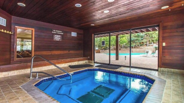 An indoor swimming pool with a wooden interior, a glass door leading outside, and a sign indicating no children under 18 allowed. - Pinetree Retreat - Hot Tub, Heated Pool & Sauna - 6 Min Walk to Dining & Lift (Park City)